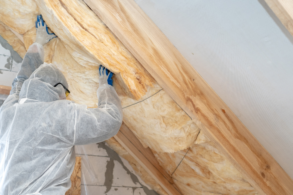 Construction worker thermally insulating house attic with glass wool